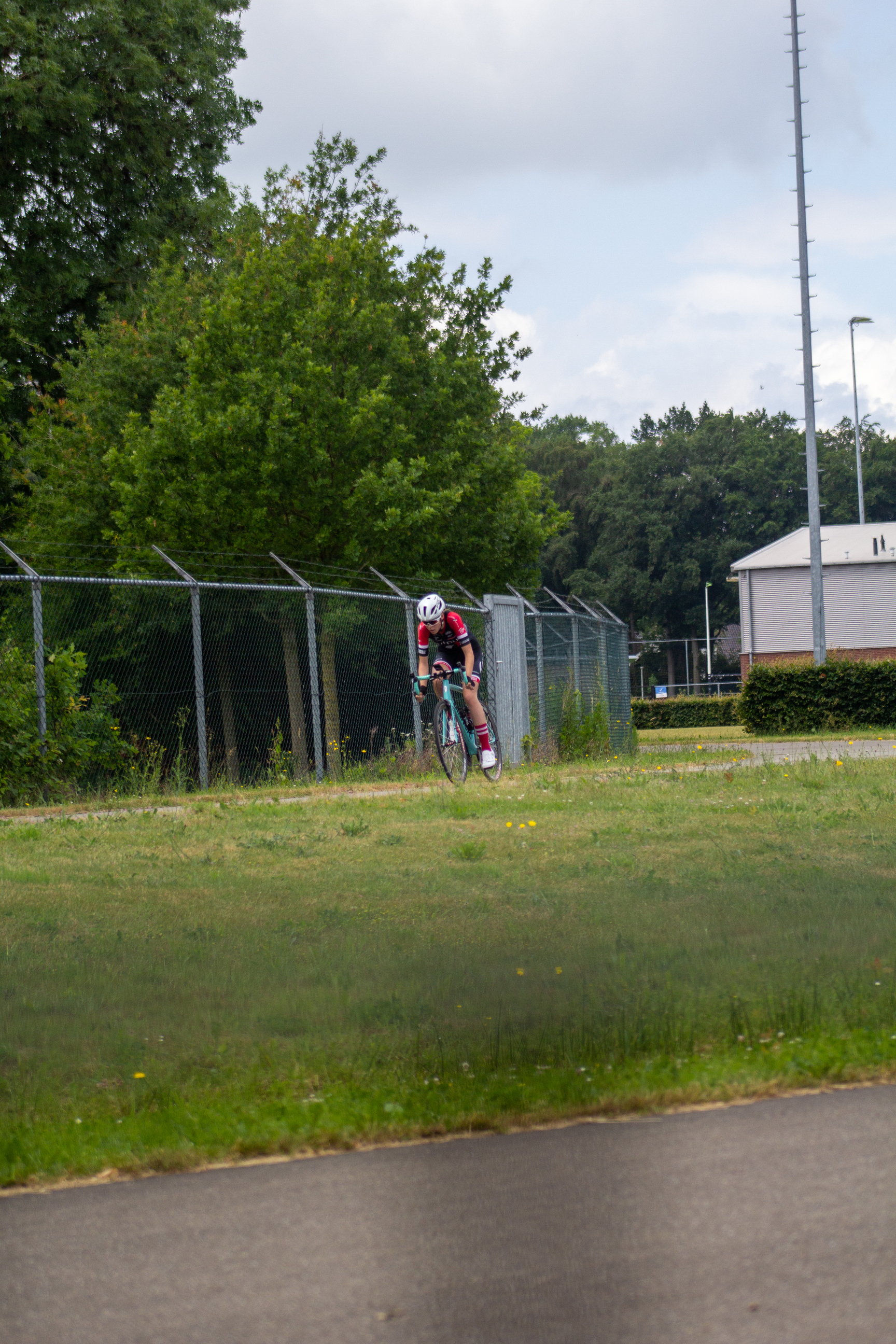 A man in a red and white shirt rides his bike along a fence.