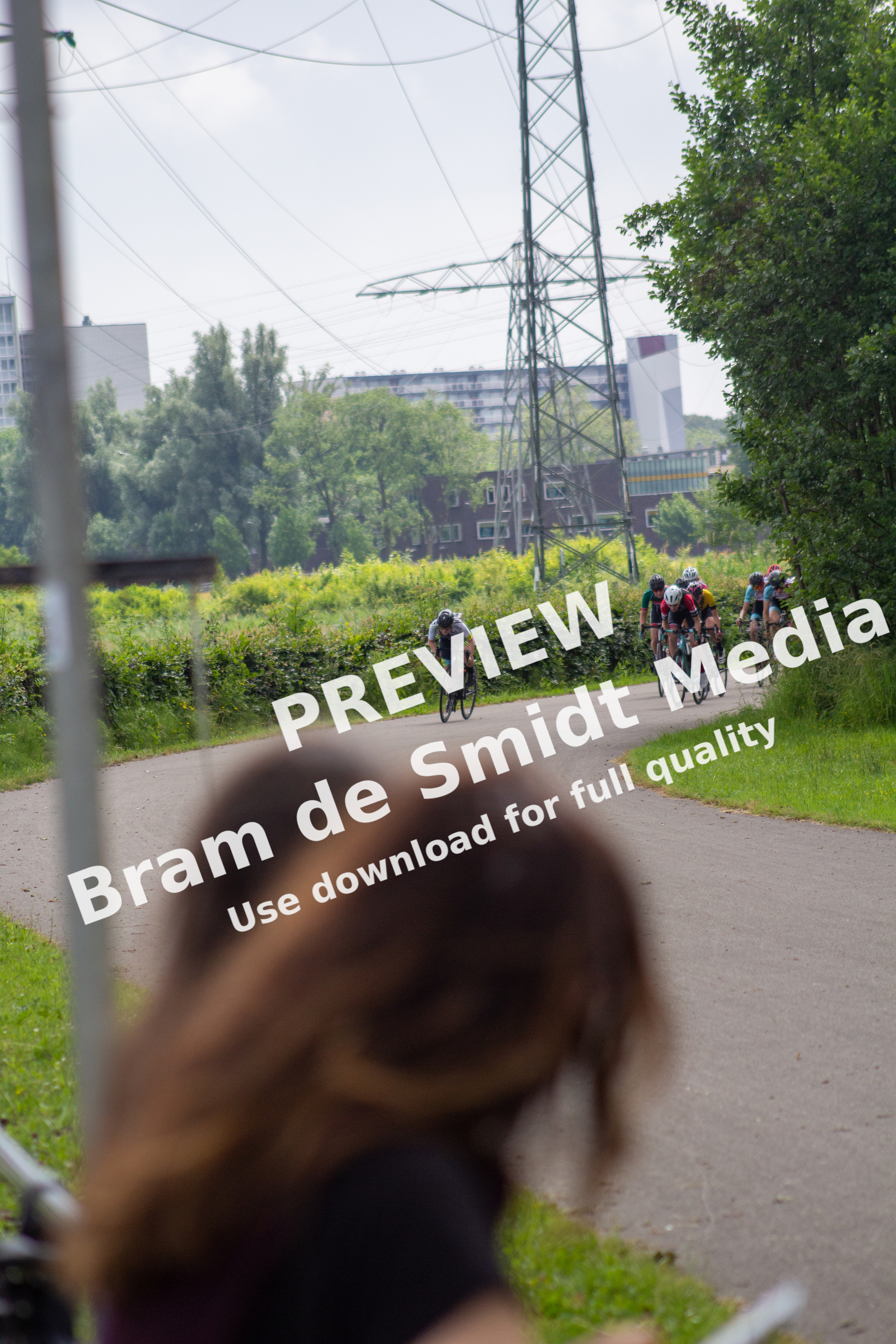 A woman watches a group of cyclists go by on a road.