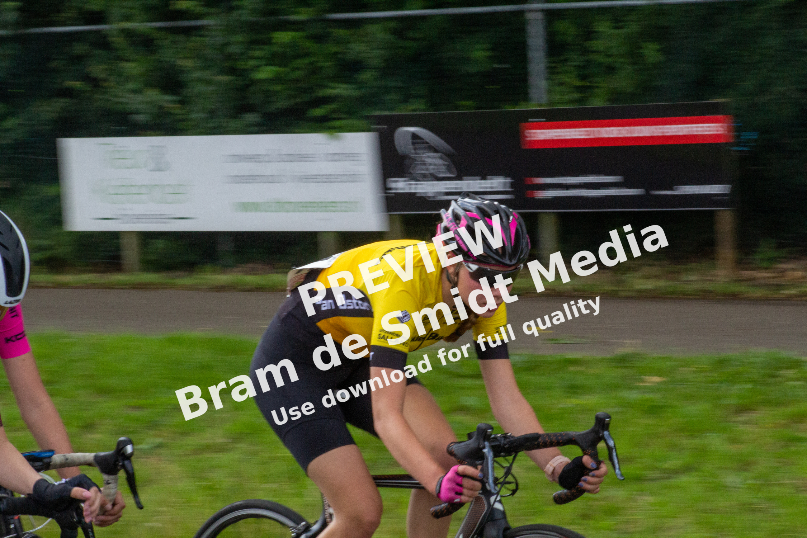 A women cycling wearing a yellow shirt with the word "Racer" written on it, riding on a road.