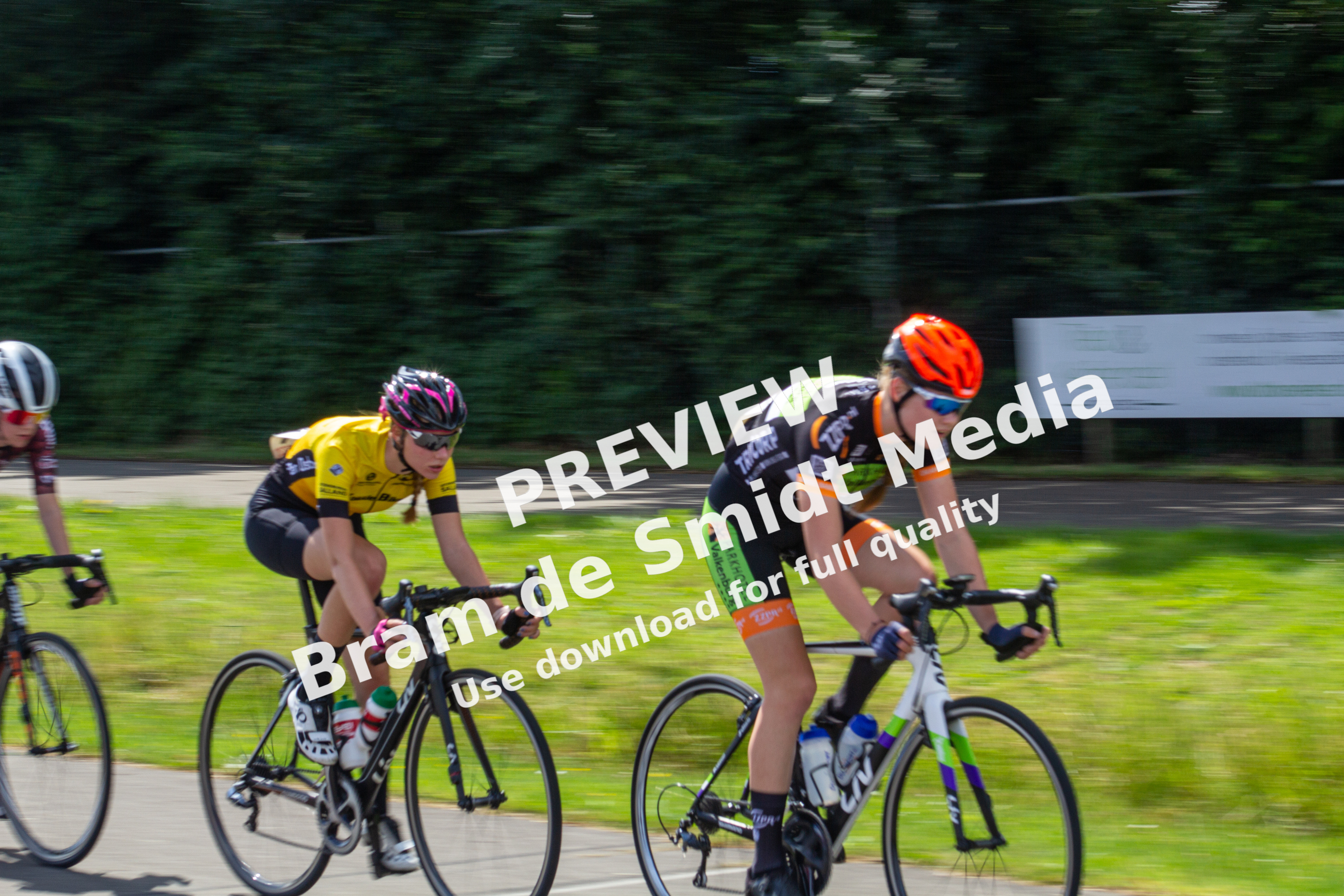 Two cyclists racing in a race and one is wearing an orange helmet.