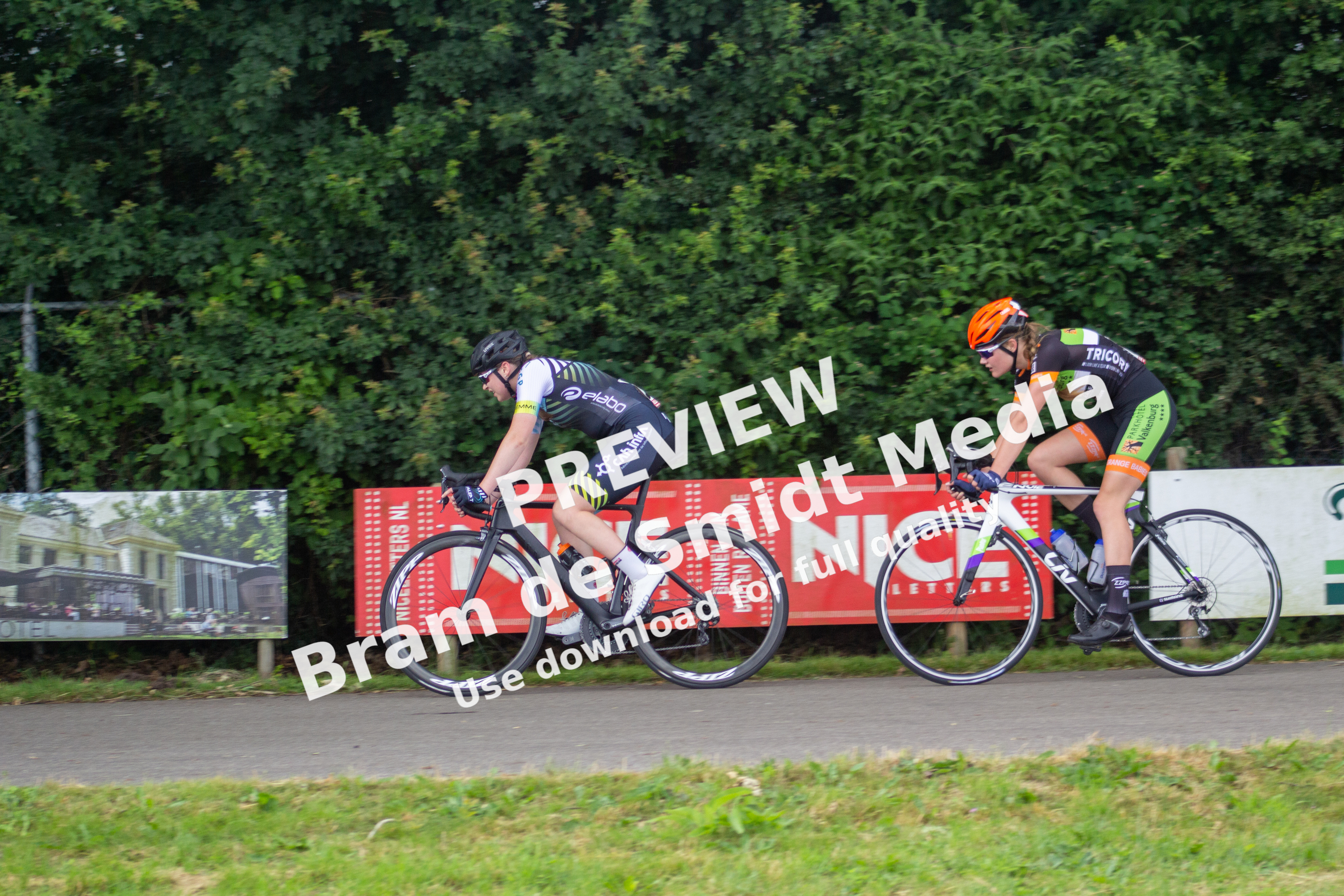 Two cyclists wearing numbers and riding on the street.