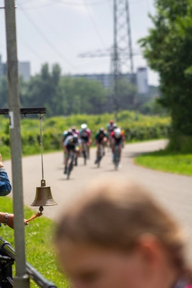 A woman wearing a pink shirt stands in front of a crowd watching cyclists race.