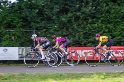 Four cyclists race down the street in a women's cycling event.