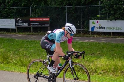 A female cyclist wearing a pink and blue uniform is riding her bike on the road.