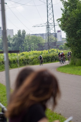 A woman watches a group of cyclists go by on a road.