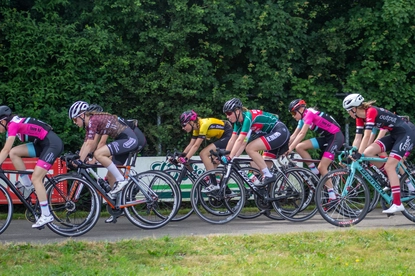 Six women participating in a bicycle race, all wearing helmets and riding identical blue bikes.