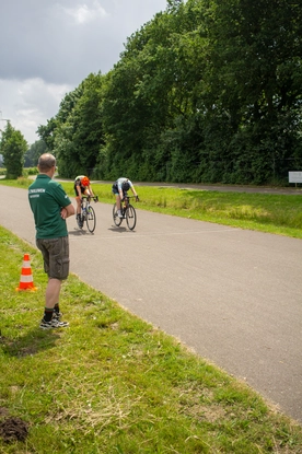 Three cyclists are riding on the road as one man looks on.