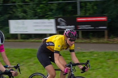 A women cycling wearing a yellow shirt with the word "Racer" written on it, riding on a road.