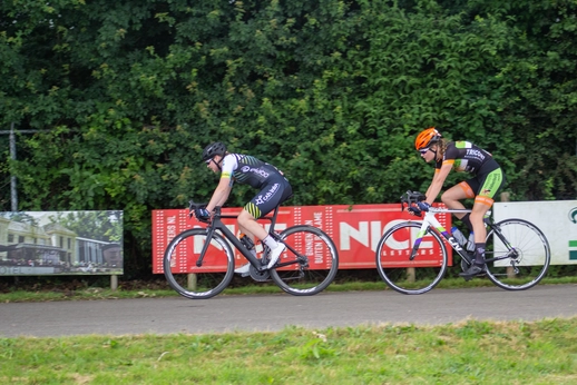 Two cyclists wearing numbers and riding on the street.