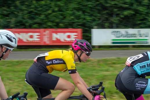 Three cyclists on a track with banners for Nice and Wielrennen.