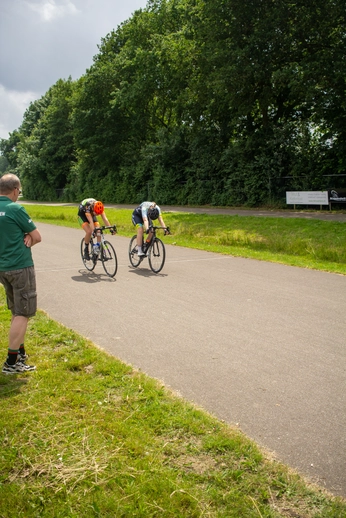 Wielrennen, Dames ronde van Deventer. The image depicts two cyclists riding on a road with trees and grass in the background.