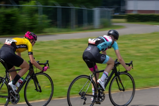 Two women are riding bikes in a race. One is wearing a yellow shirt and the other is in blue.