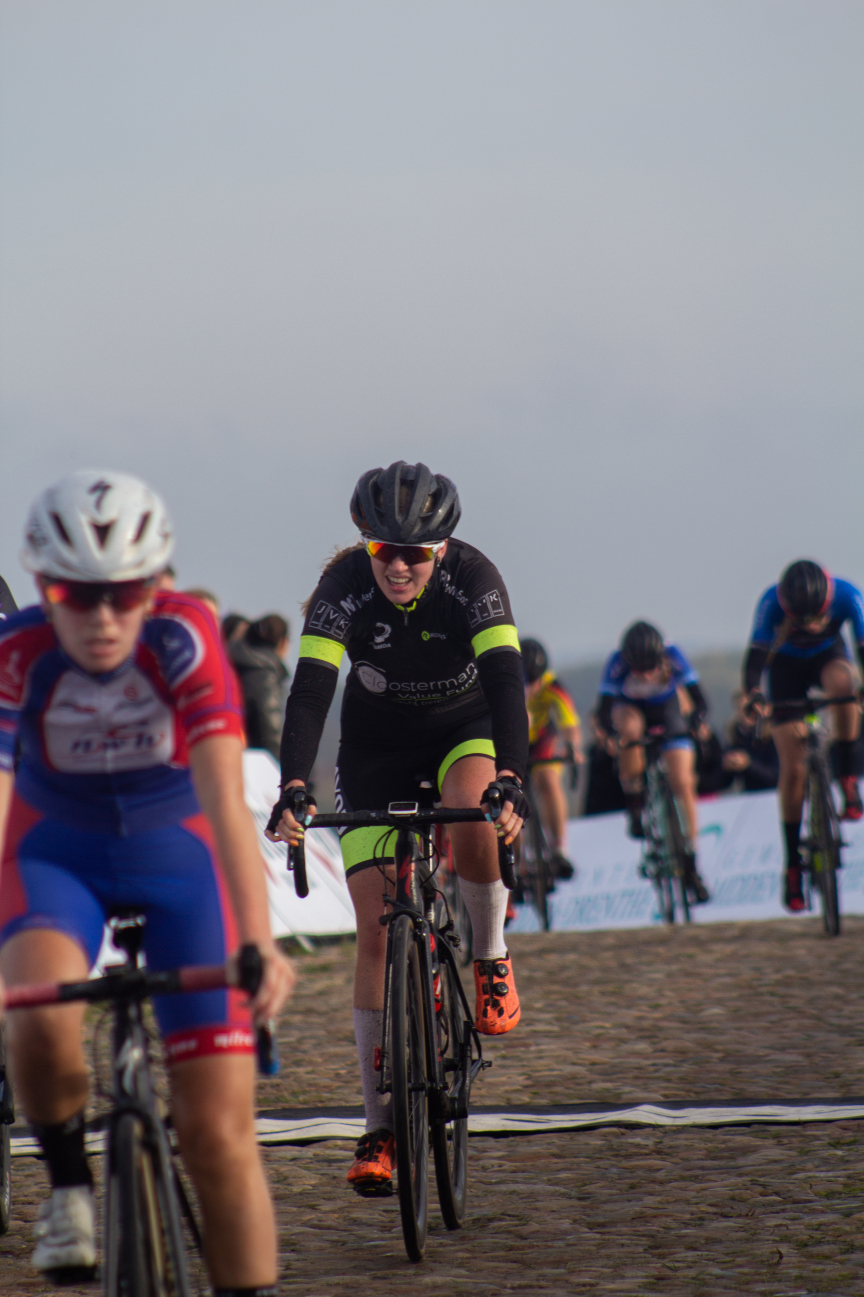 A group of people participate in a bicycle race on a cobblestone road.