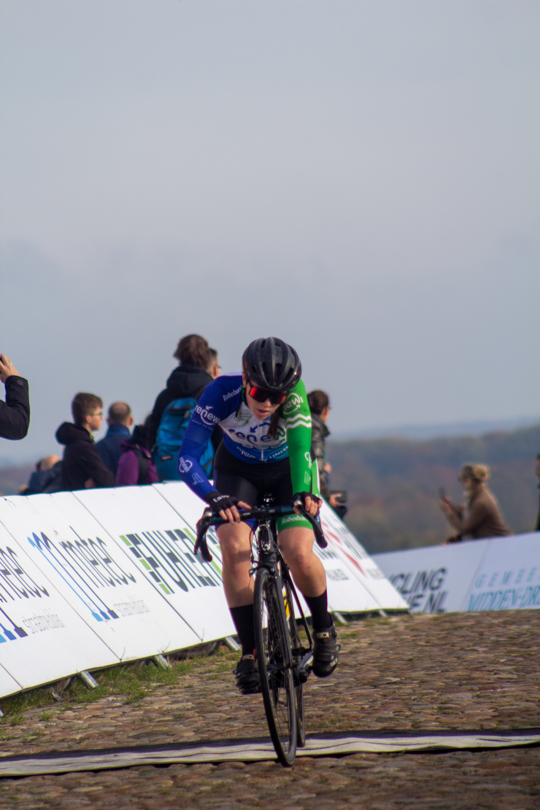 A cyclist wearing a blue and white top is riding on the cobblestone street in NK Nieuweling.