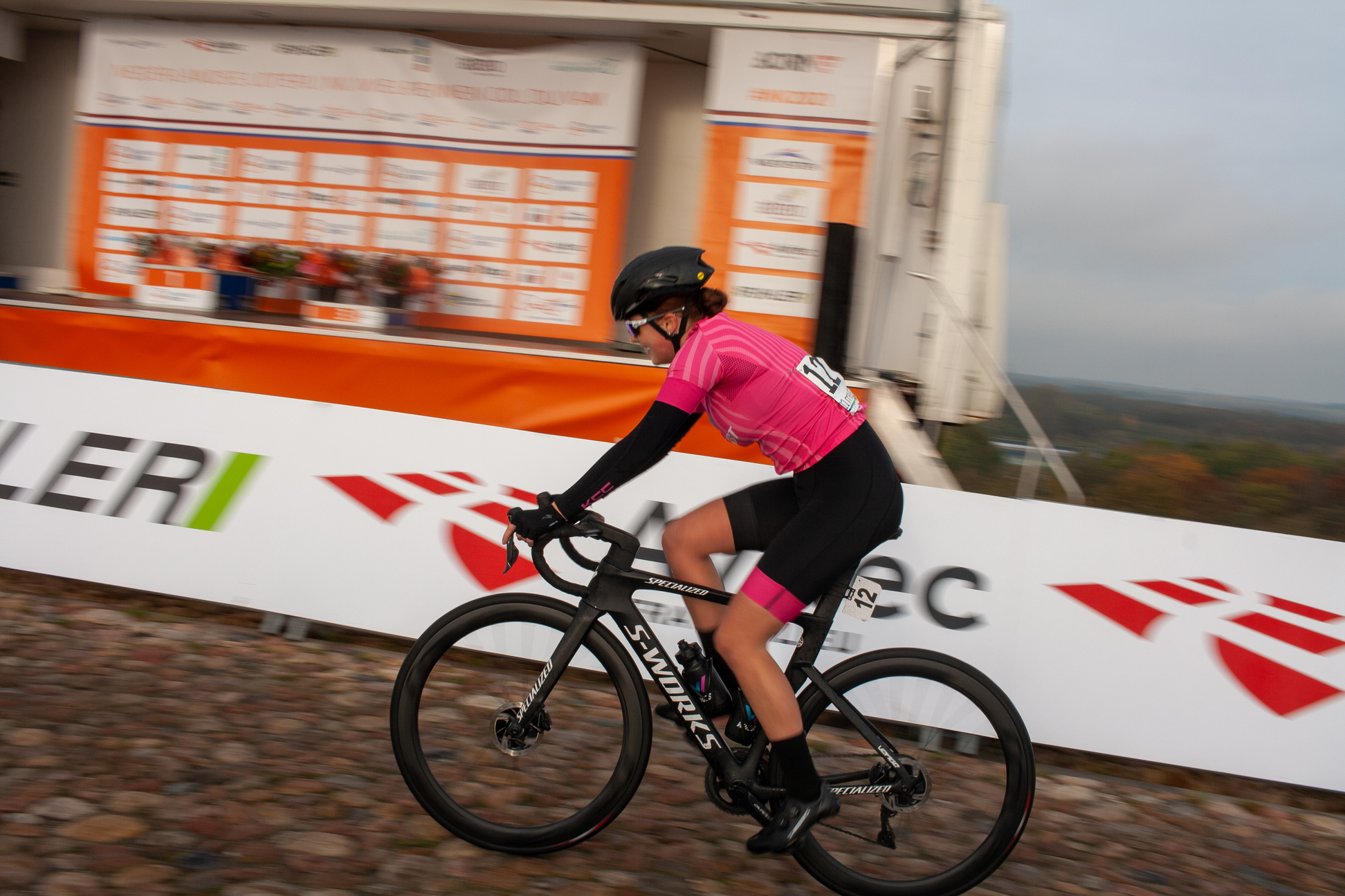 A female cyclist wearing a pink jersey and black pants is riding her bike down the road.