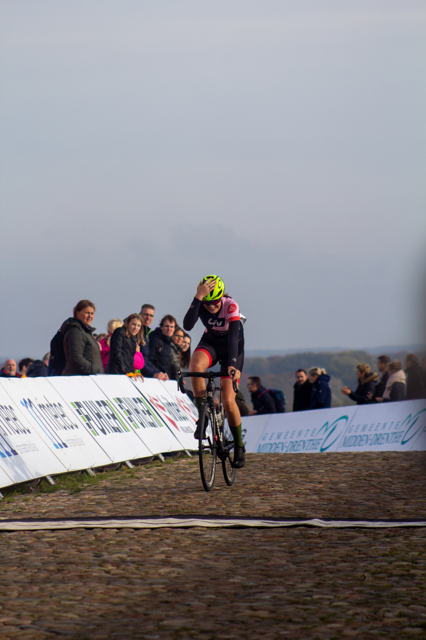 A cyclist wearing a yellow helmet and pink outfit racing in a race.