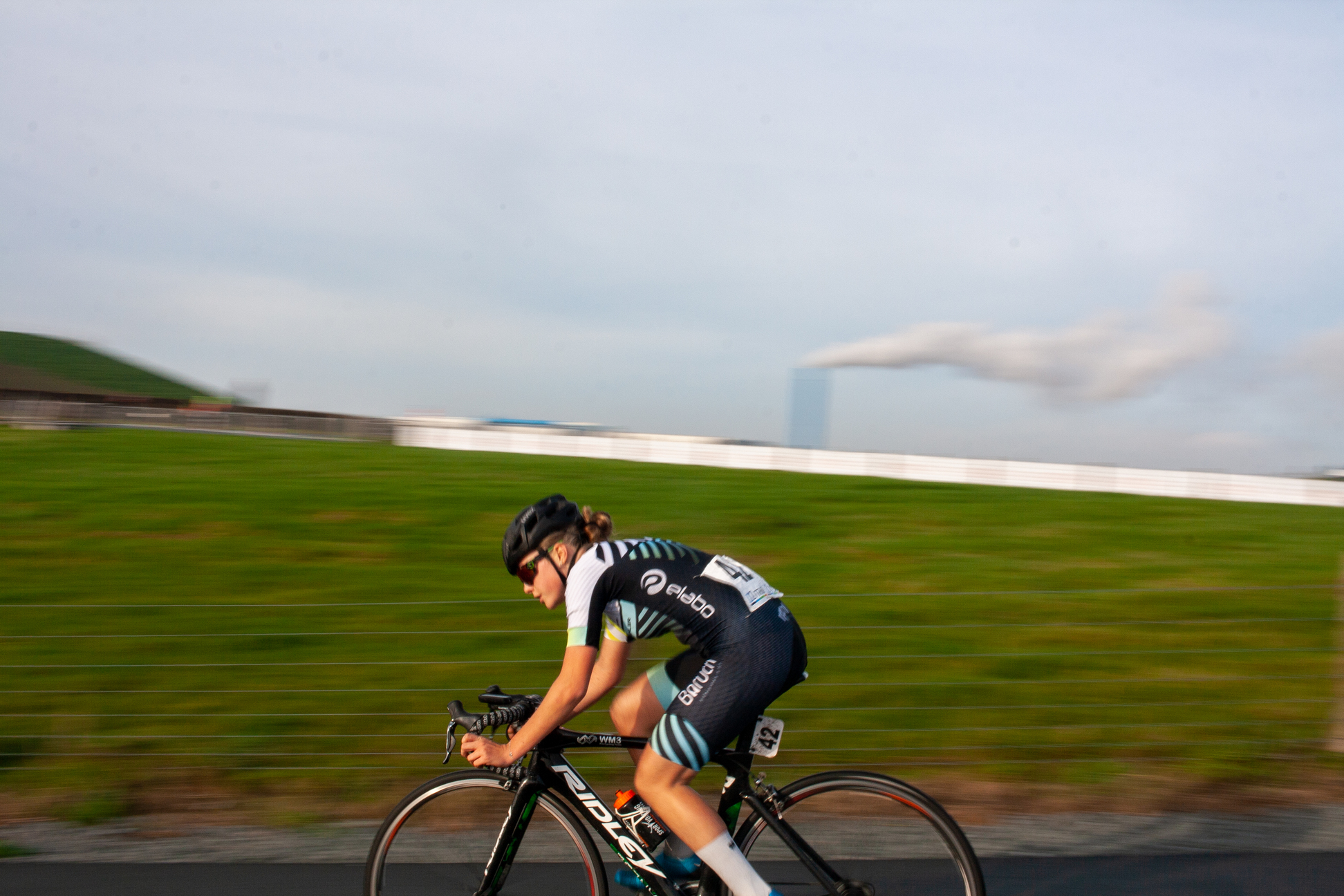 A woman wears a blue Wielrennen jersey while riding her bike.