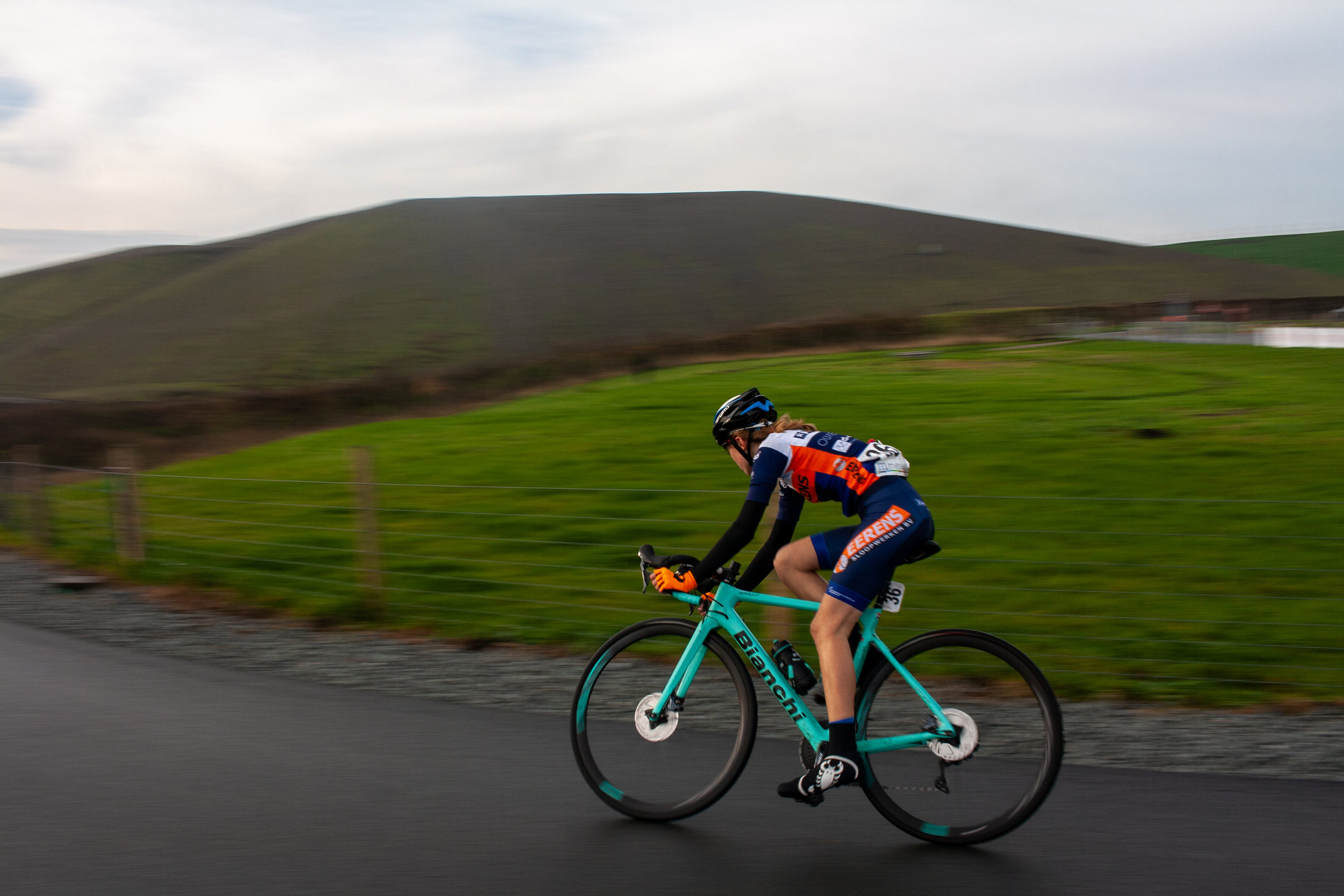 A man in a racing suit is riding his blue bicycle on the road.