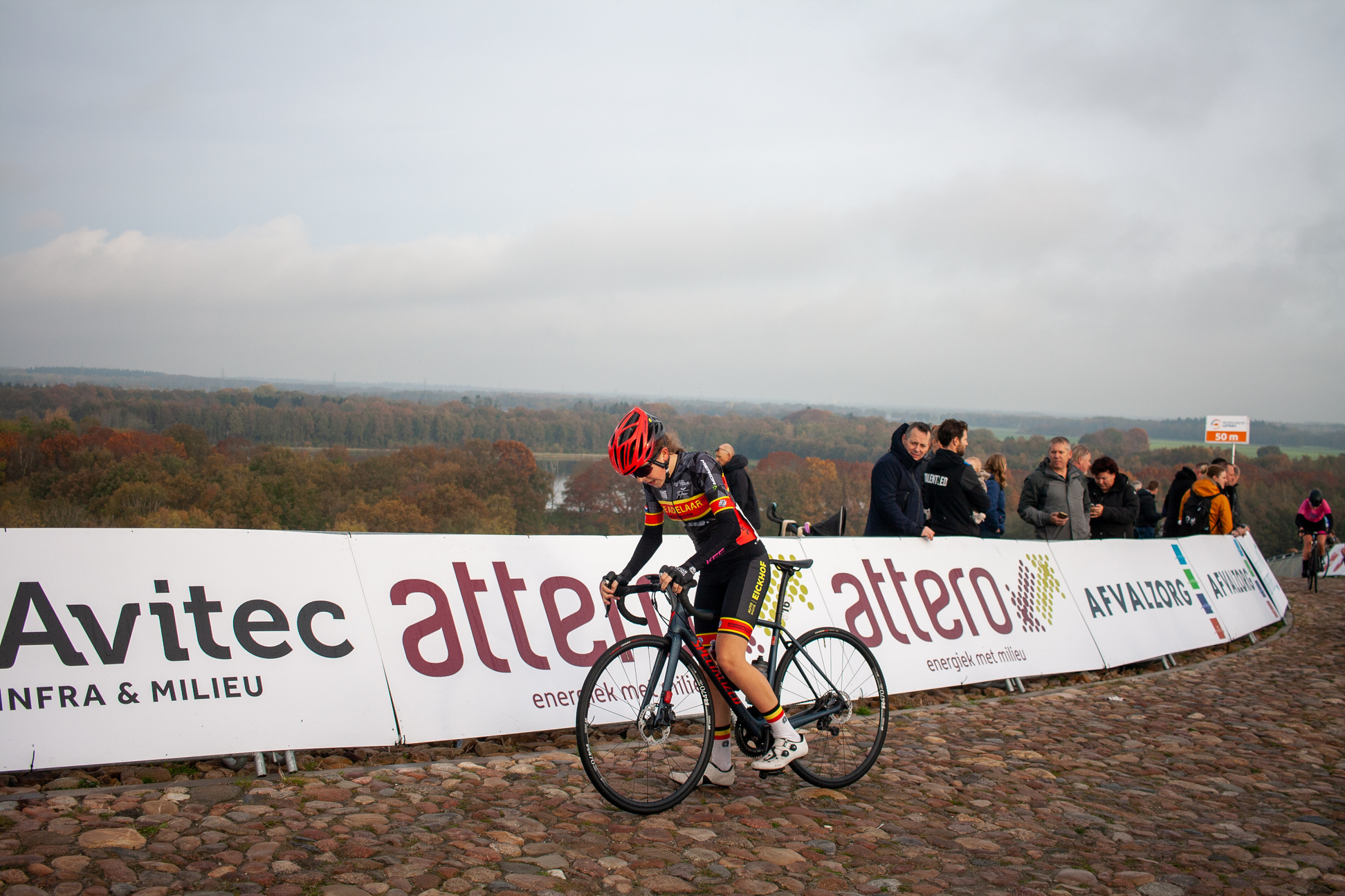 A person in a red helmet is riding a bicycle on cobblestones.