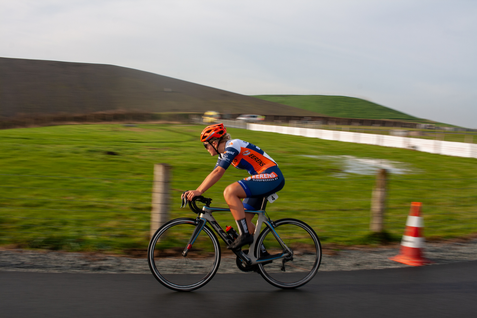 A male cyclist is riding a bike down the road with an NK logo on his jersey and blue cap.