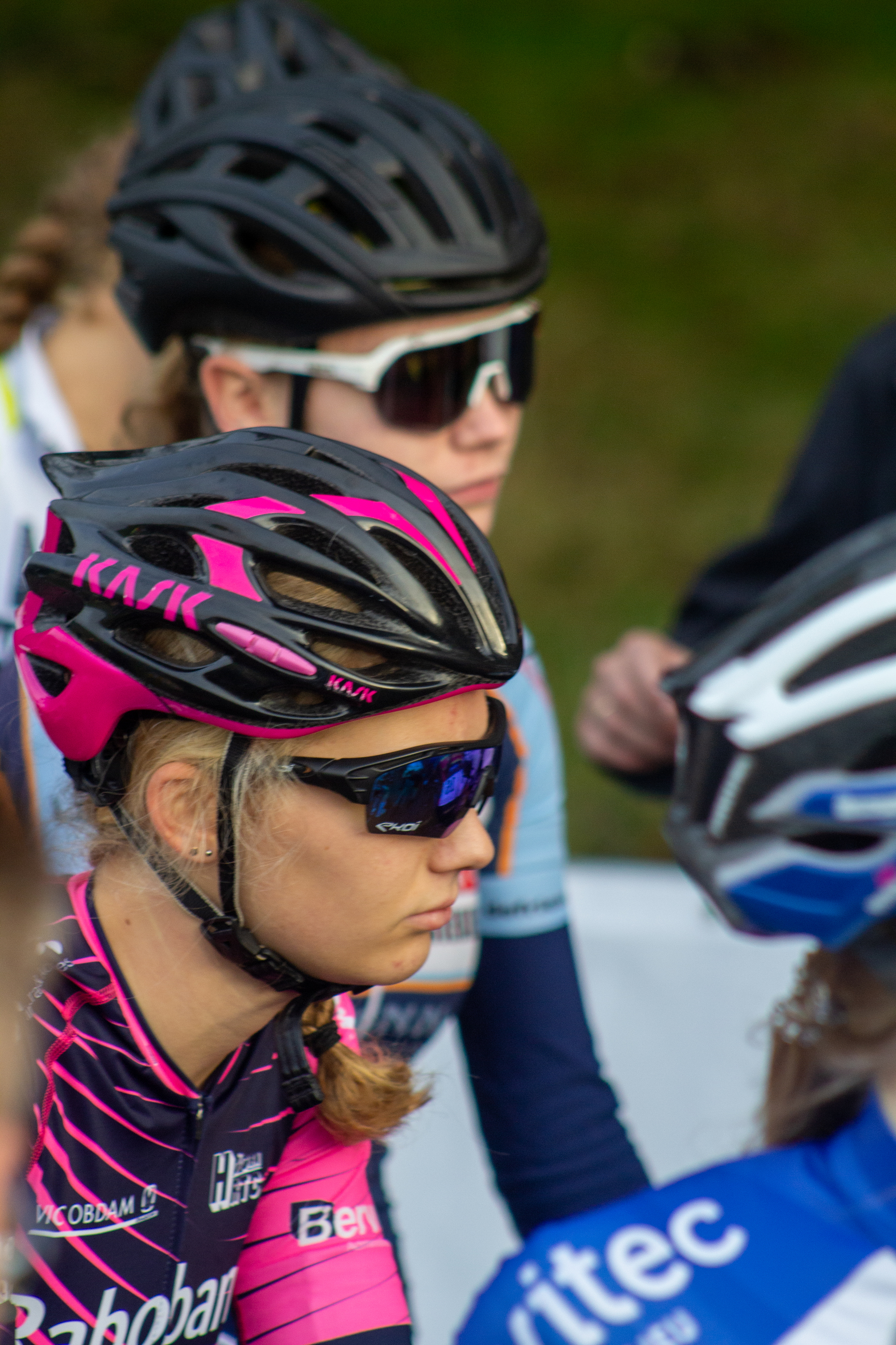 A woman wearing a pink bib with the name "NK Nieuweling" on it is part of a group of cyclists.