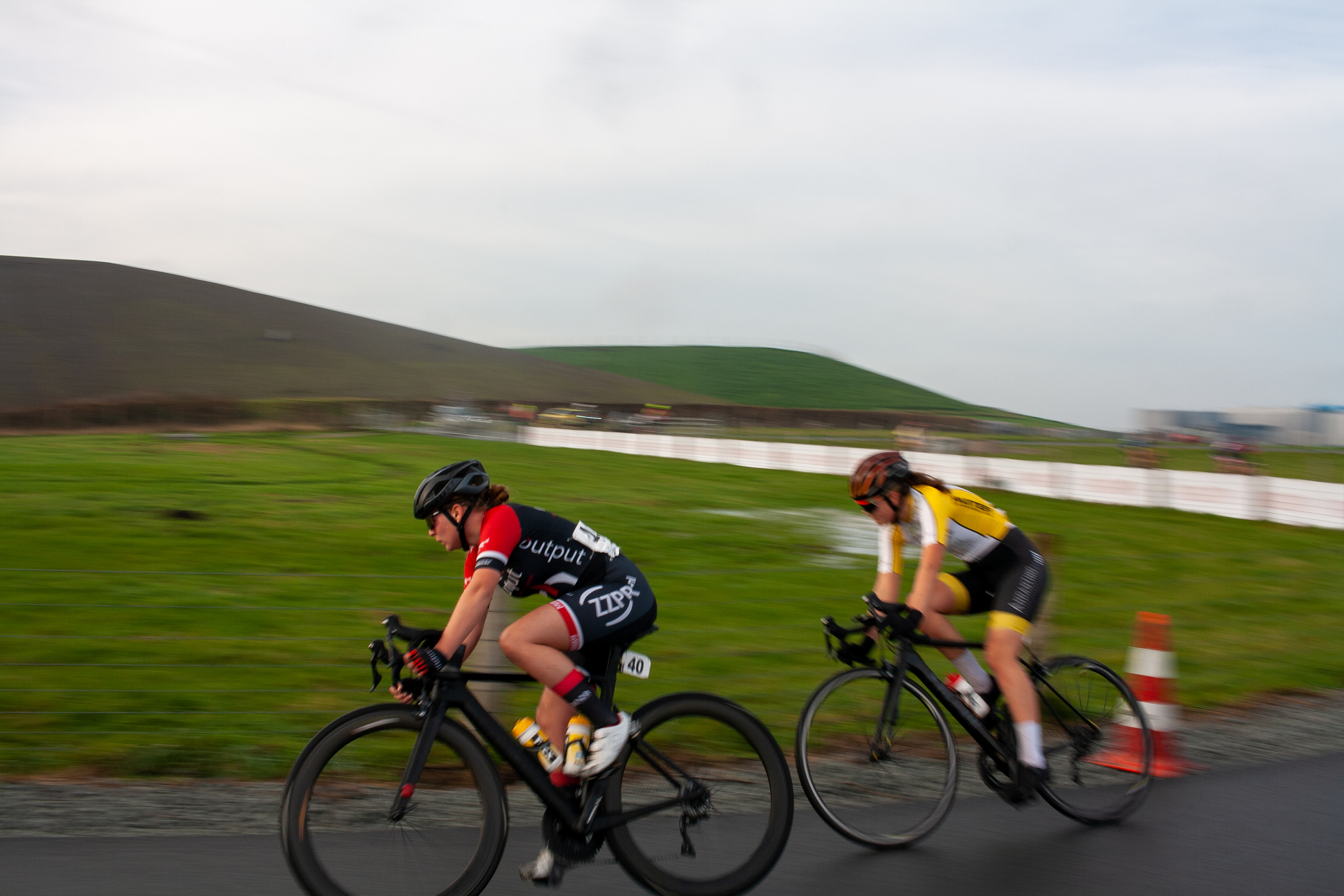 Two women riding bikes on a road with one wearing the number 4.