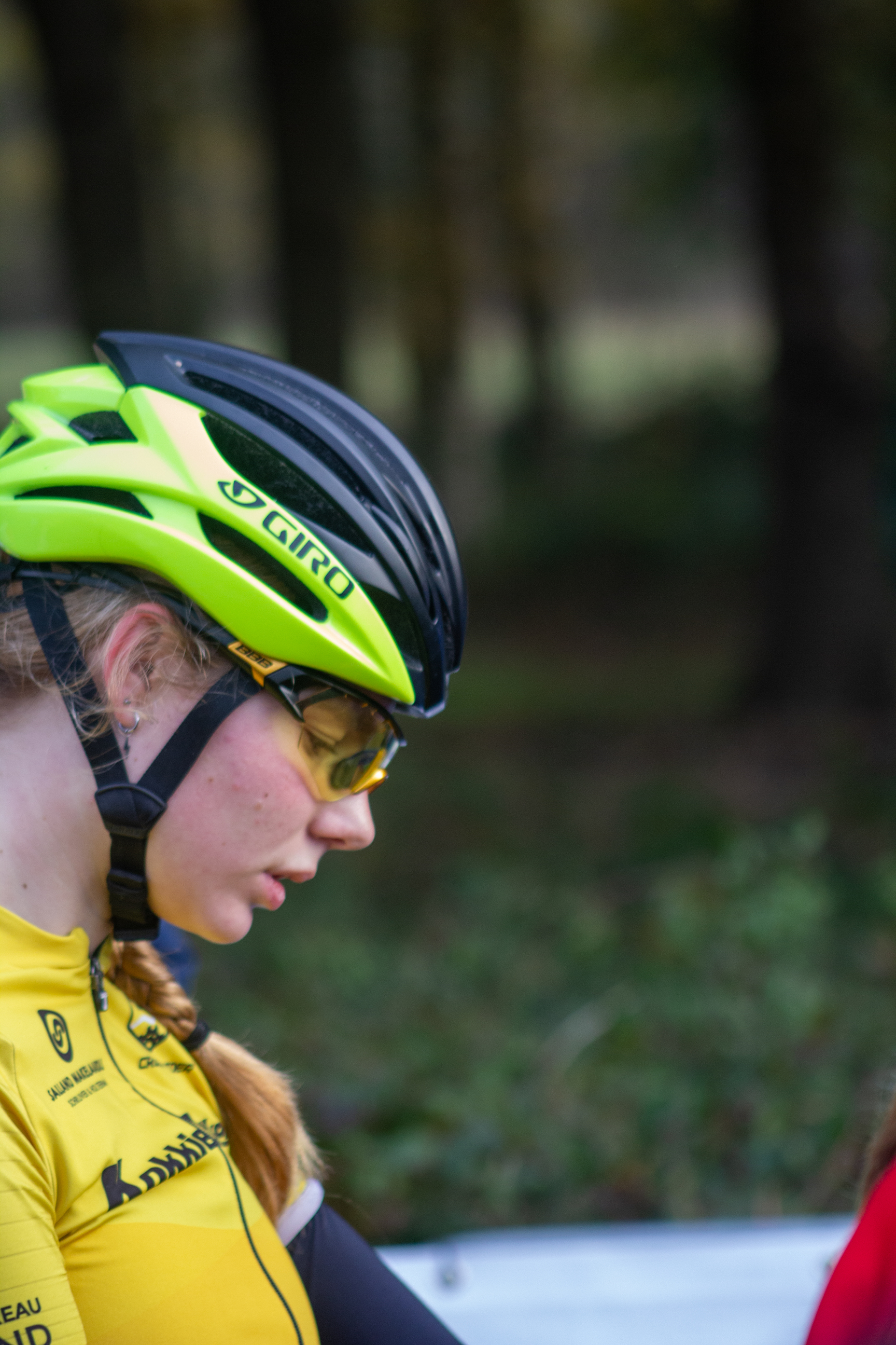 A woman with a yellow shirt and a green helmet stands looking towards the left.