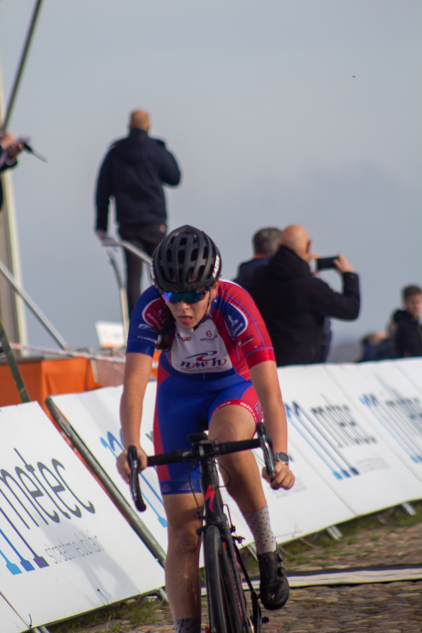 A young cyclist is riding in a race, her jersey reading NK Nieuweling.