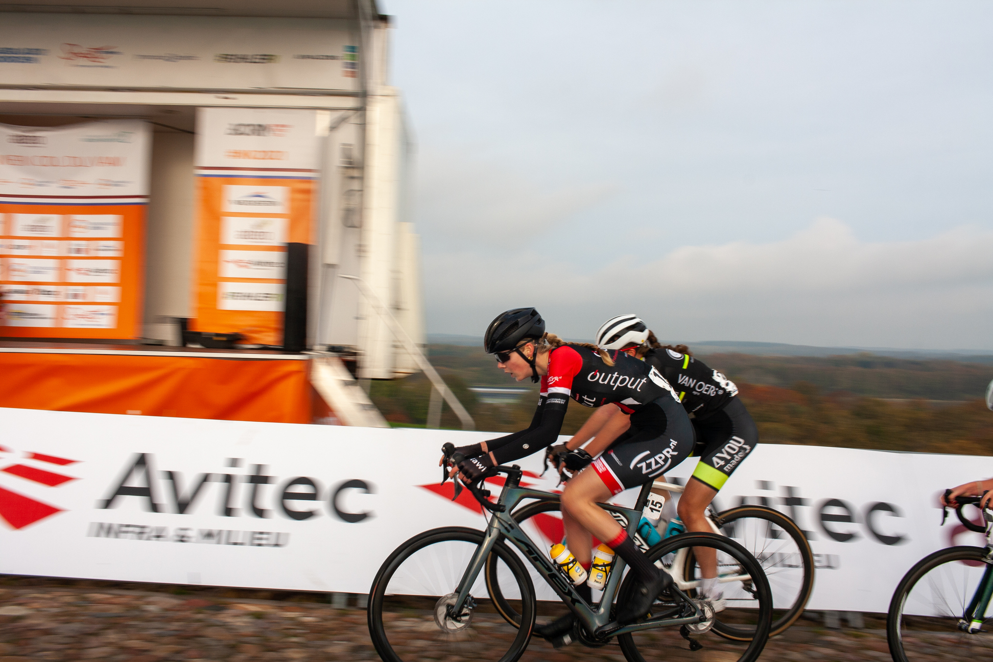 Two cyclists racing on a track sponsored by Avitec.