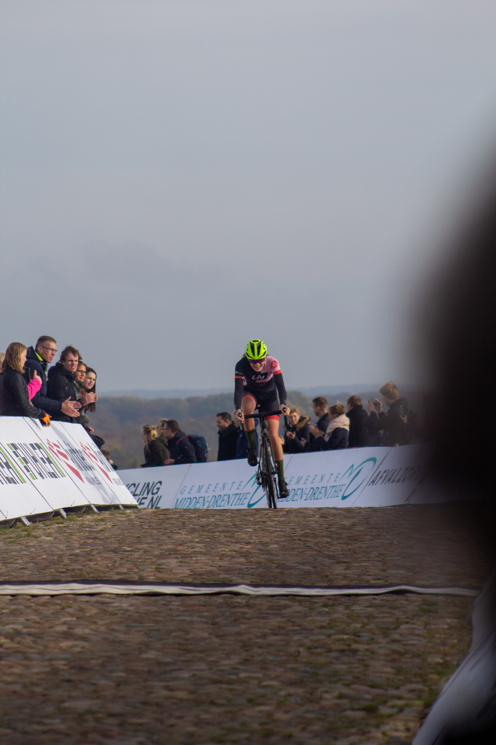 A cyclist wearing a yellow helmet is on the track during a race sponsored by NK Nieuweling.