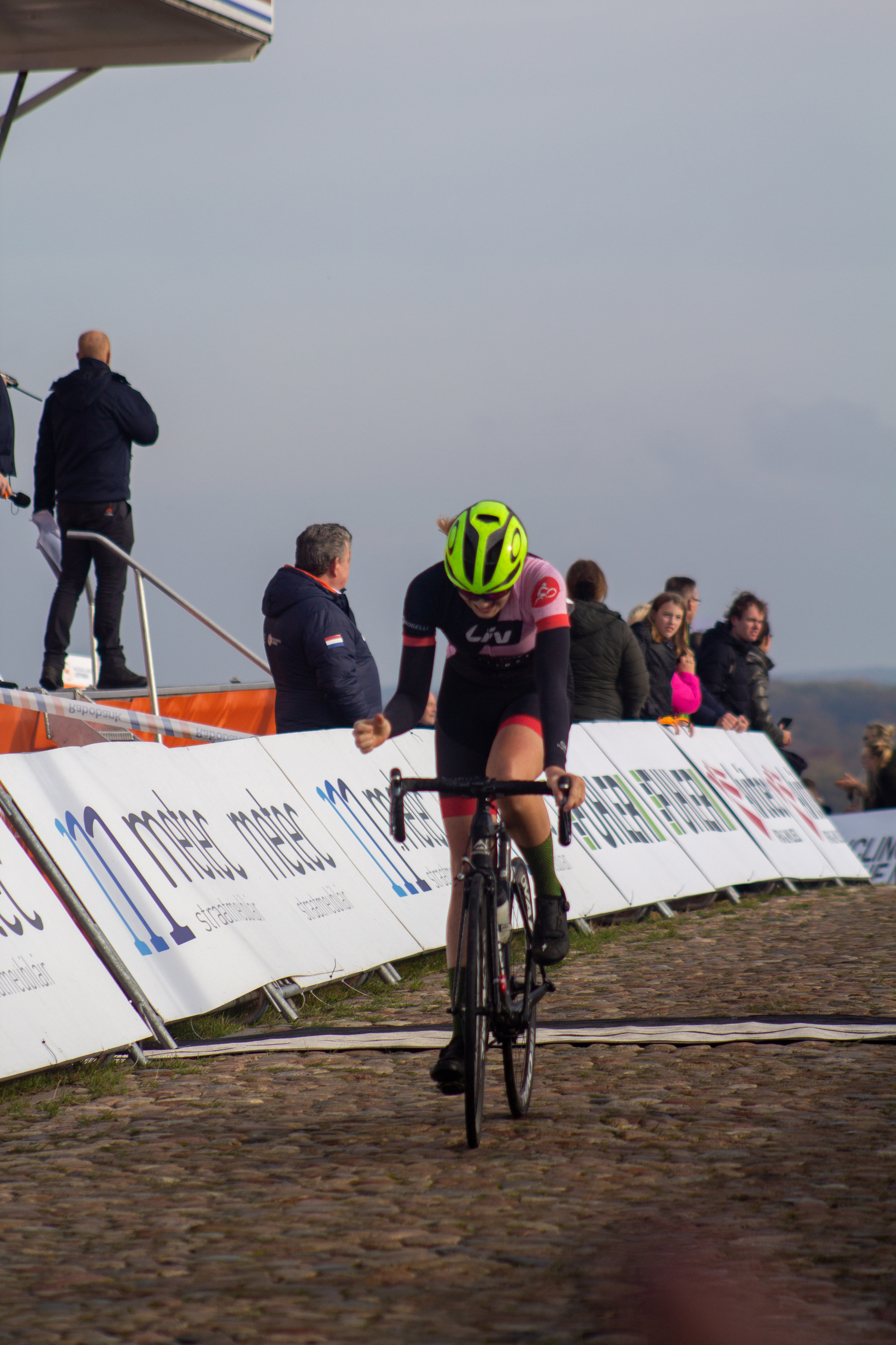 A woman wearing a helmet is riding her bicycle through a cobblestone road at the NK Nieuweling Dames race.