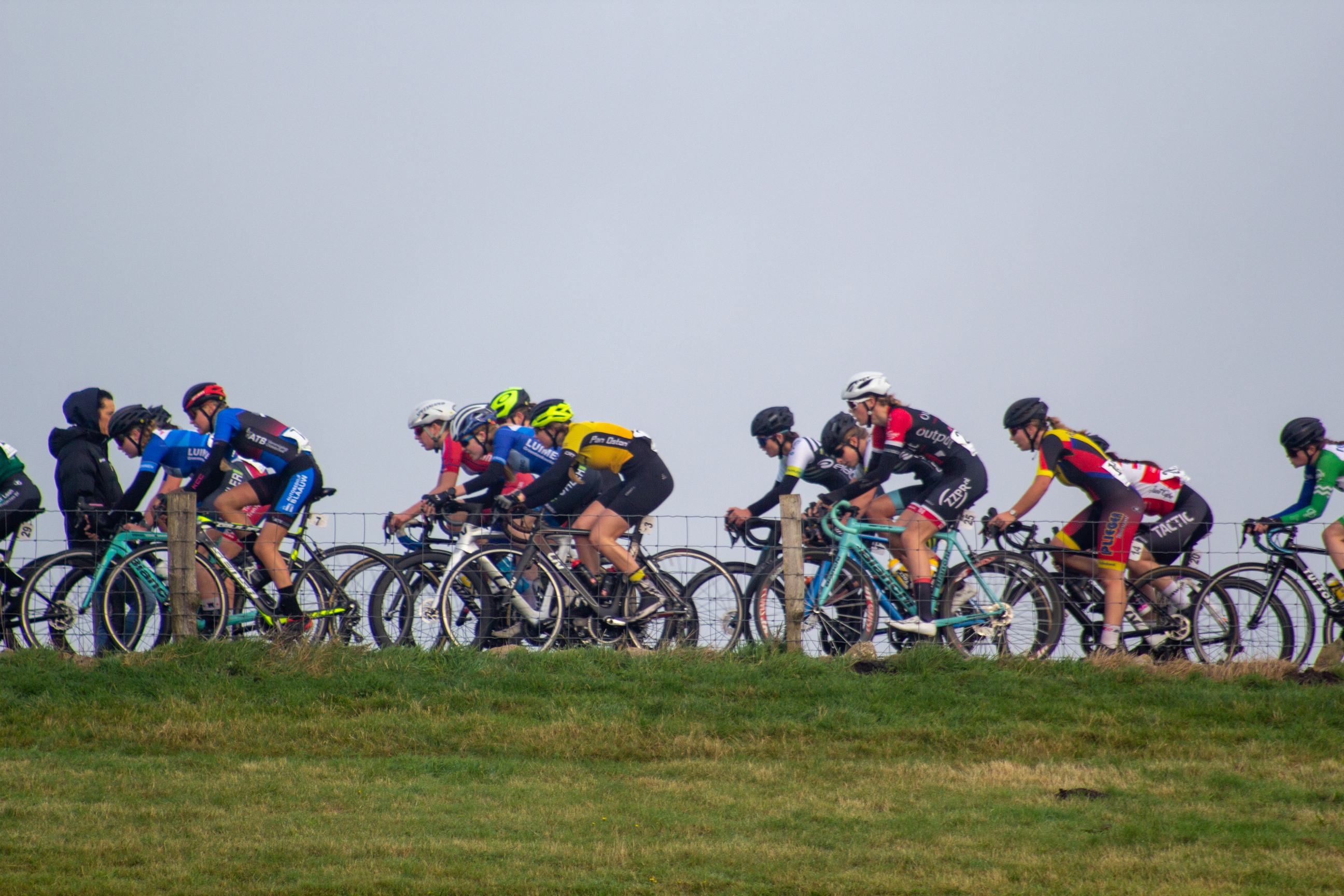 A group of cyclists riding on a grassy hillside with one person standing on the side.