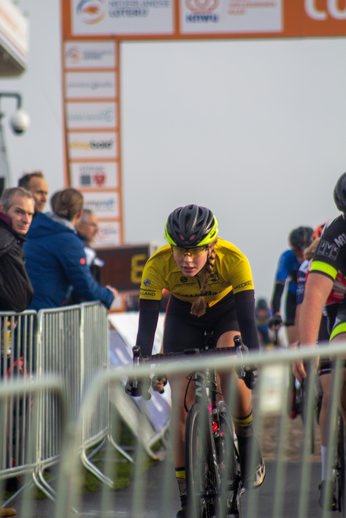 A cyclist wearing a yellow shirt is racing down the road.