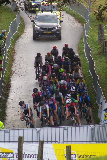 A group of cyclists race down a narrow road as spectators watch from the side.