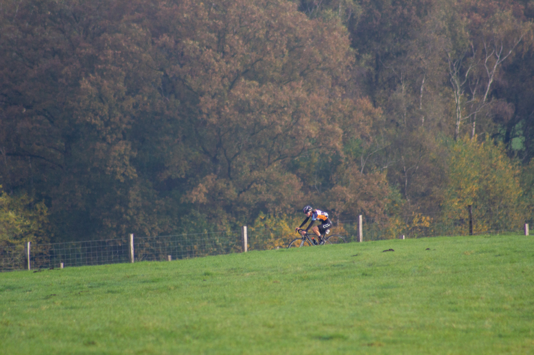 A cyclist in a blue and black jersey riding a bike across a field.