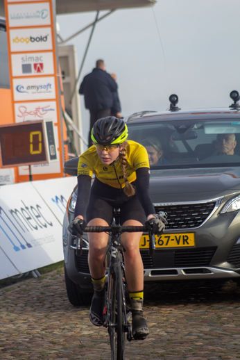 A woman in a yellow shirt and black shorts is riding a bike past a car.