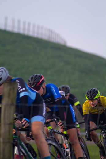 A group of cyclists on the track, with one wearing a vibrant yellow jersey.