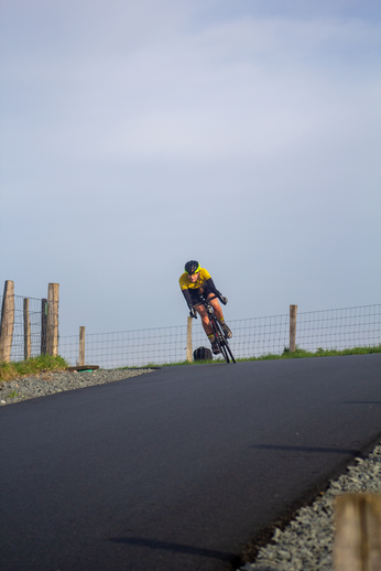 A person in a yellow and black shirt is riding a bicycle on an asphalt path.