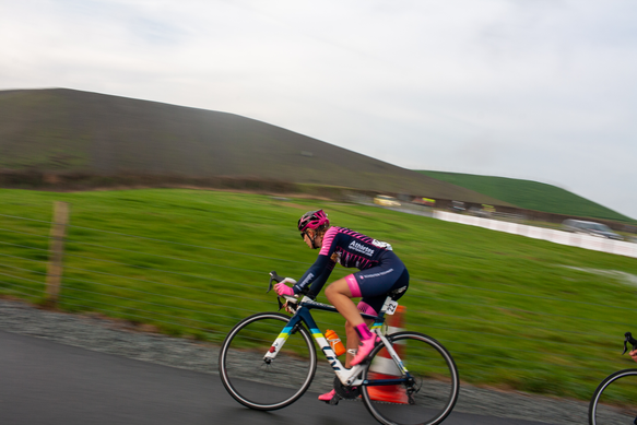 Two women on bikes, one in a pink jersey that says NK Nieuweling, the other in blue.