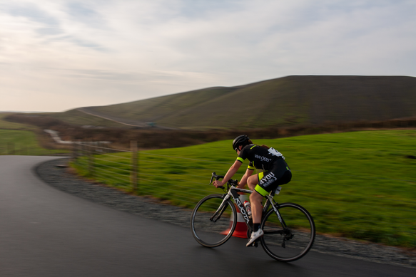 A bicycle racer wears a black jersey with 1 on it, riding down the road.