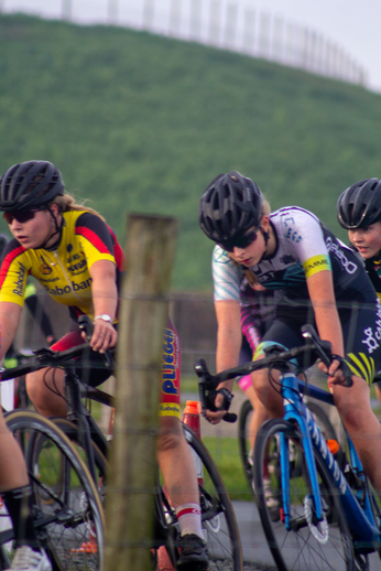 A cycling race is taking place with 3 cyclists in black and red helmets riding their bikes.