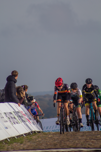 A group of cyclists with number 7 leading are racing around a bend on their bikes.