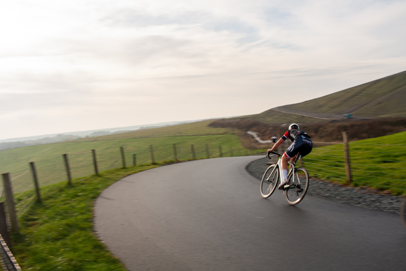 A woman riding a bike on a road. The road is made of cement and has some grass on the side.