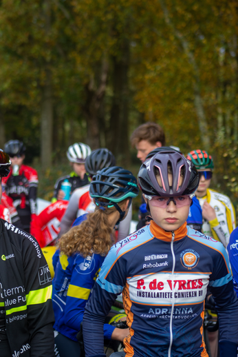 A group of cyclists are preparing for a race, with one athlete in the foreground wearing an orange helmet.