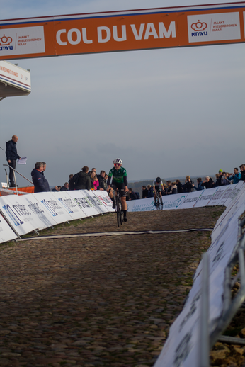 A cyclist rides down a cobblestone track with Col du Van in the background.