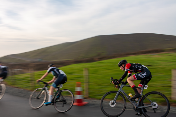 Two cyclists on a race track sponsored by Wielrennen and NK Nieuweling Dames.