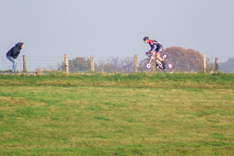 A bike racer racing on a grassy field in the NK Nieuweling Dames race.