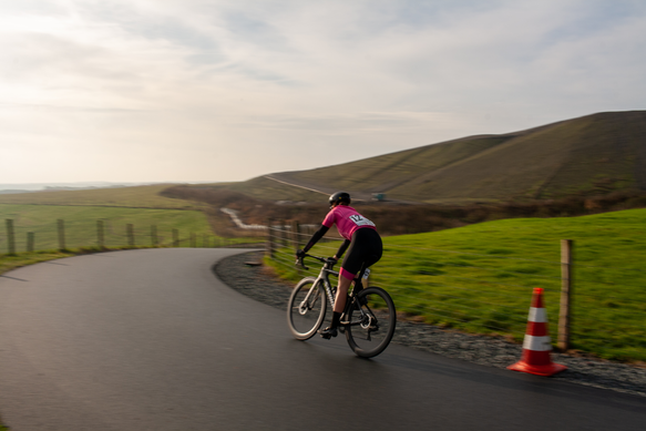 A woman wearing a pink shirt, number 11, rides her bicycle on a road.