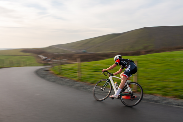 A woman wearing a black jersey and white shorts is riding a white bicycle.