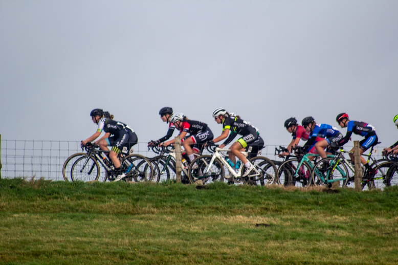 A group of cyclists, including a woman with the number 10 on her shirt, race around a grassy hill.